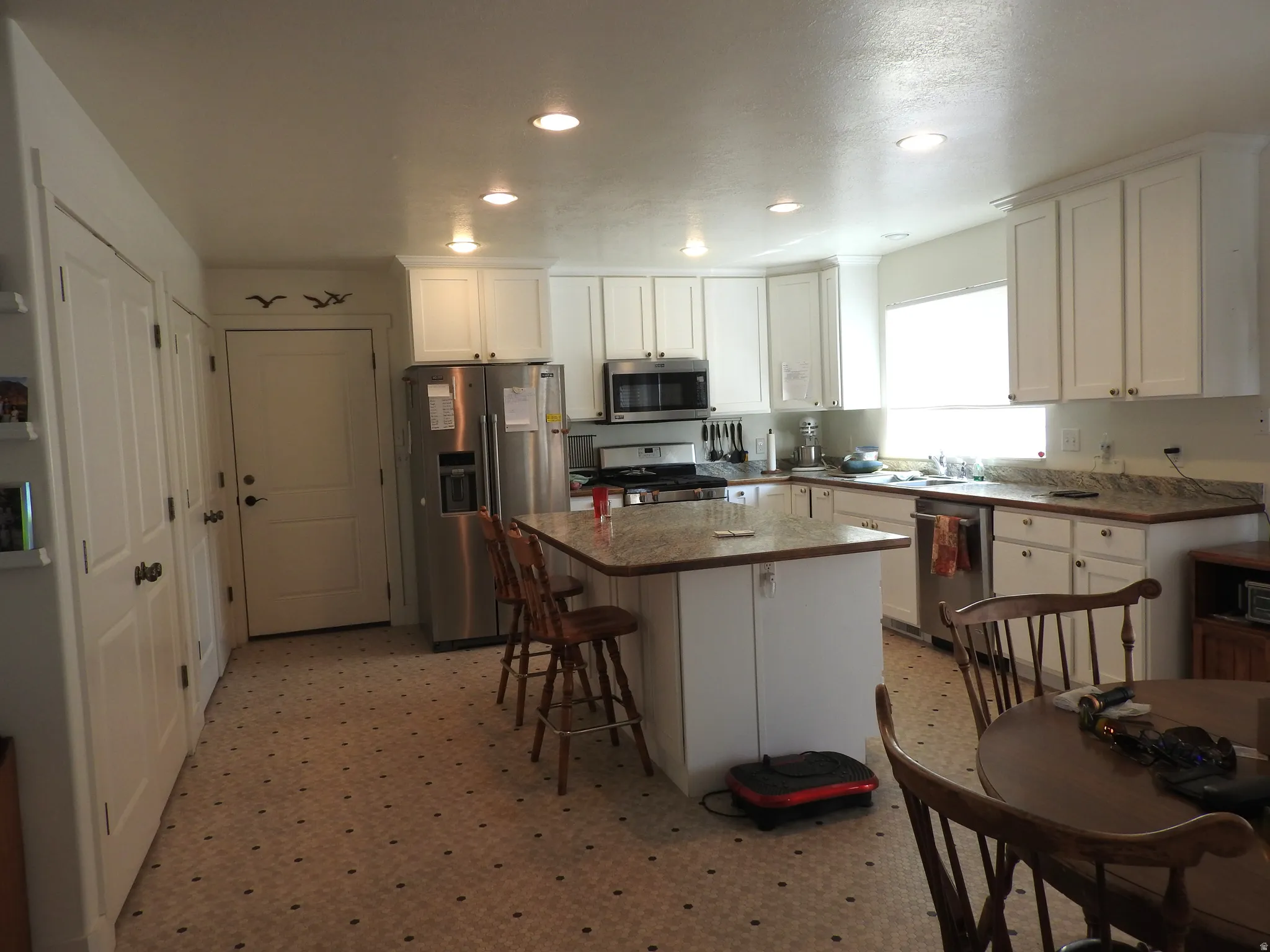 Kitchen with white cabinets, light flooring, stainless steel appliances, a kitchen breakfast bar, and a kitchen island