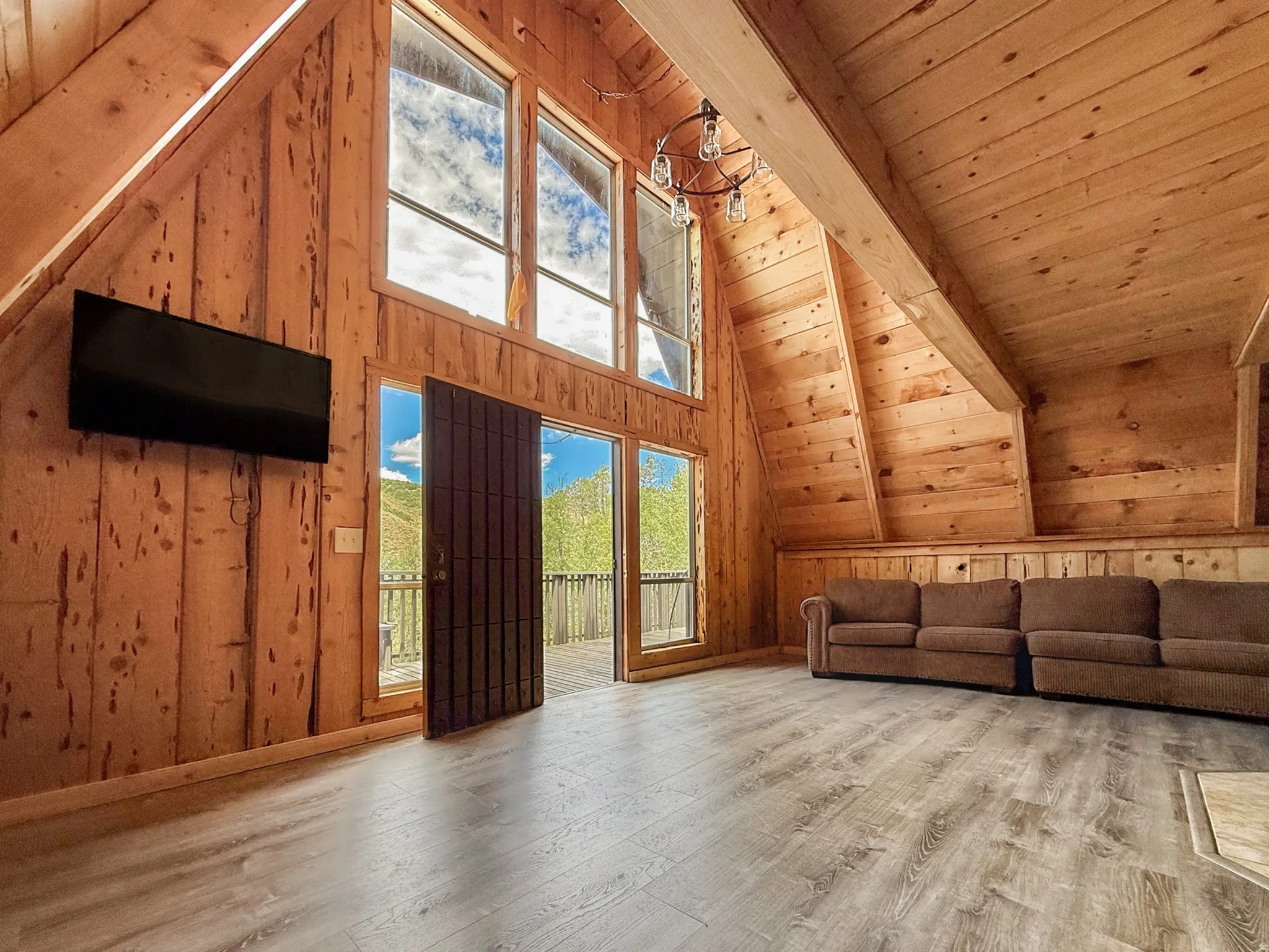Unfurnished living room with wood walls, light wood-style flooring, and a high wooden beamed ceiling