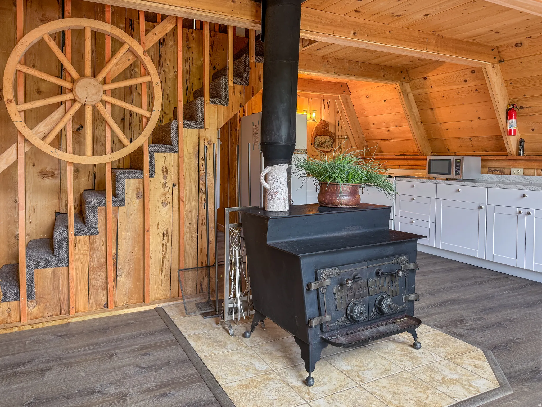 Detailed view of a wood stove, stainless steel microwave, wood finished floors, and a wooden ceiling with exposed beams