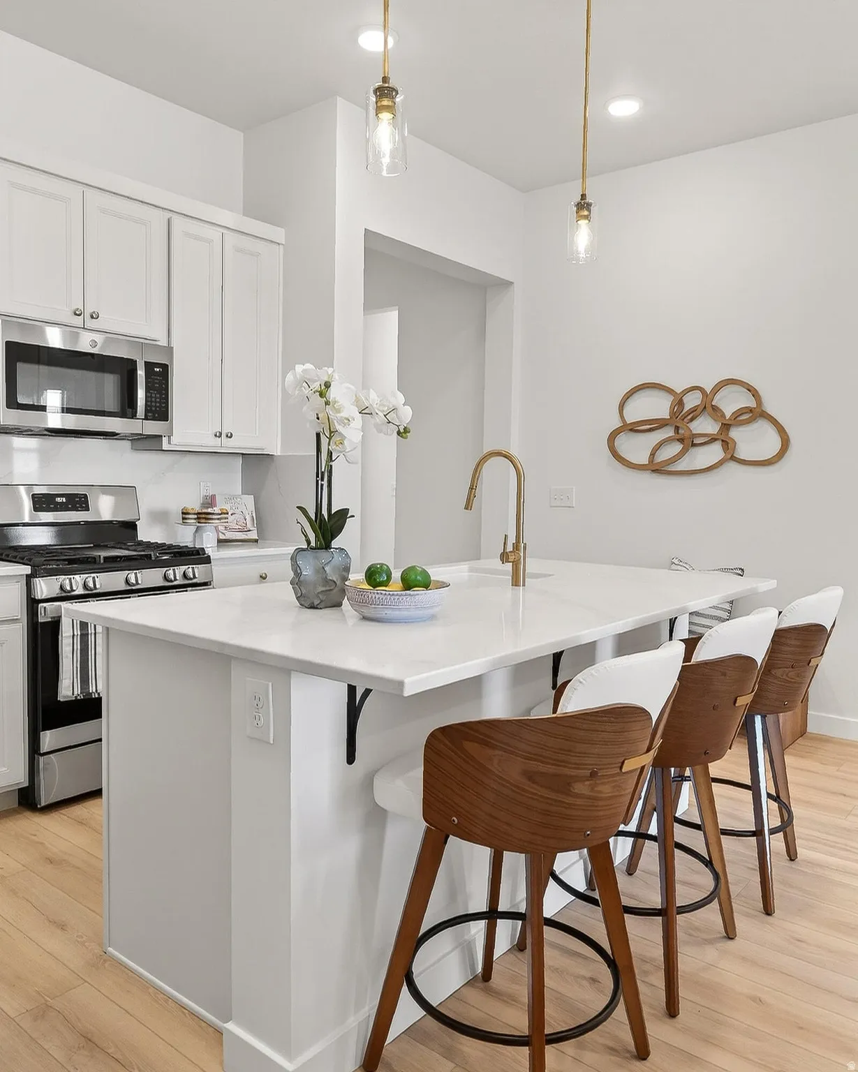 Kitchen with stainless steel appliances, light wood-style flooring, white cabinets, hanging light fixtures, and a center island with sink