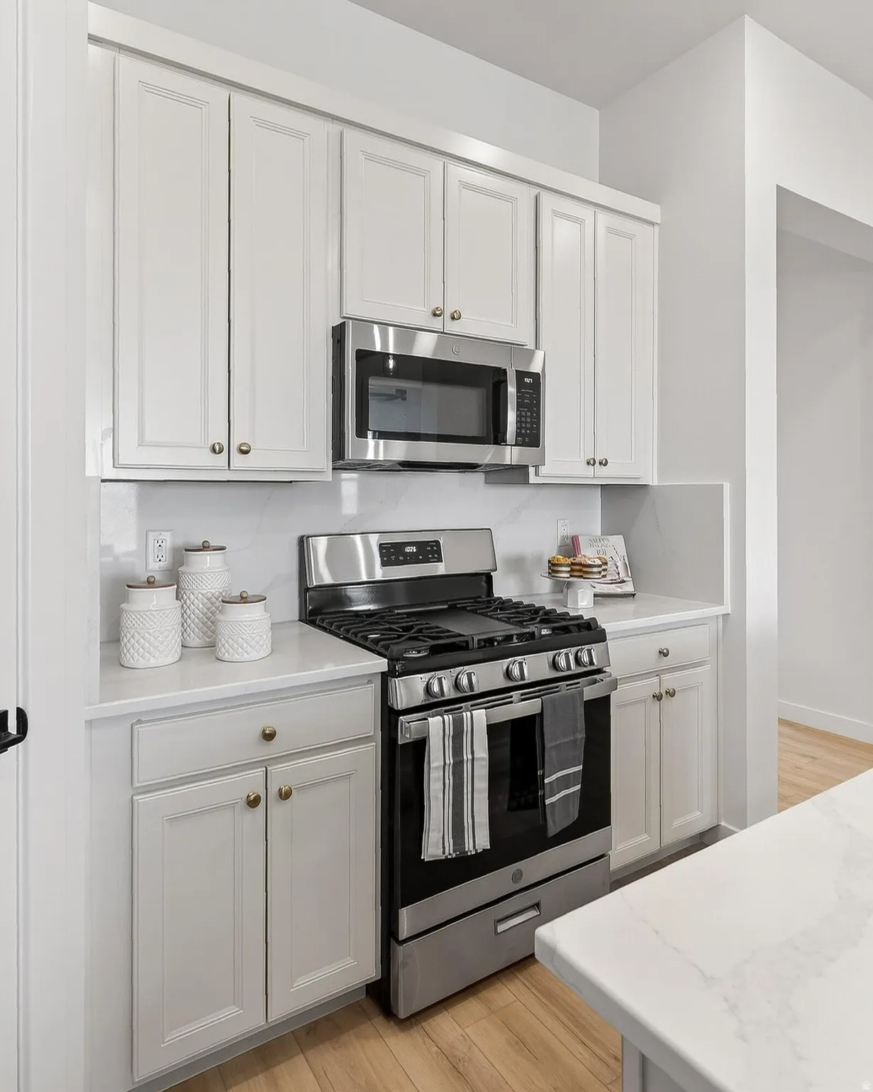 Kitchen with stainless steel appliances, light wood-style flooring, white cabinets, and light stone counters