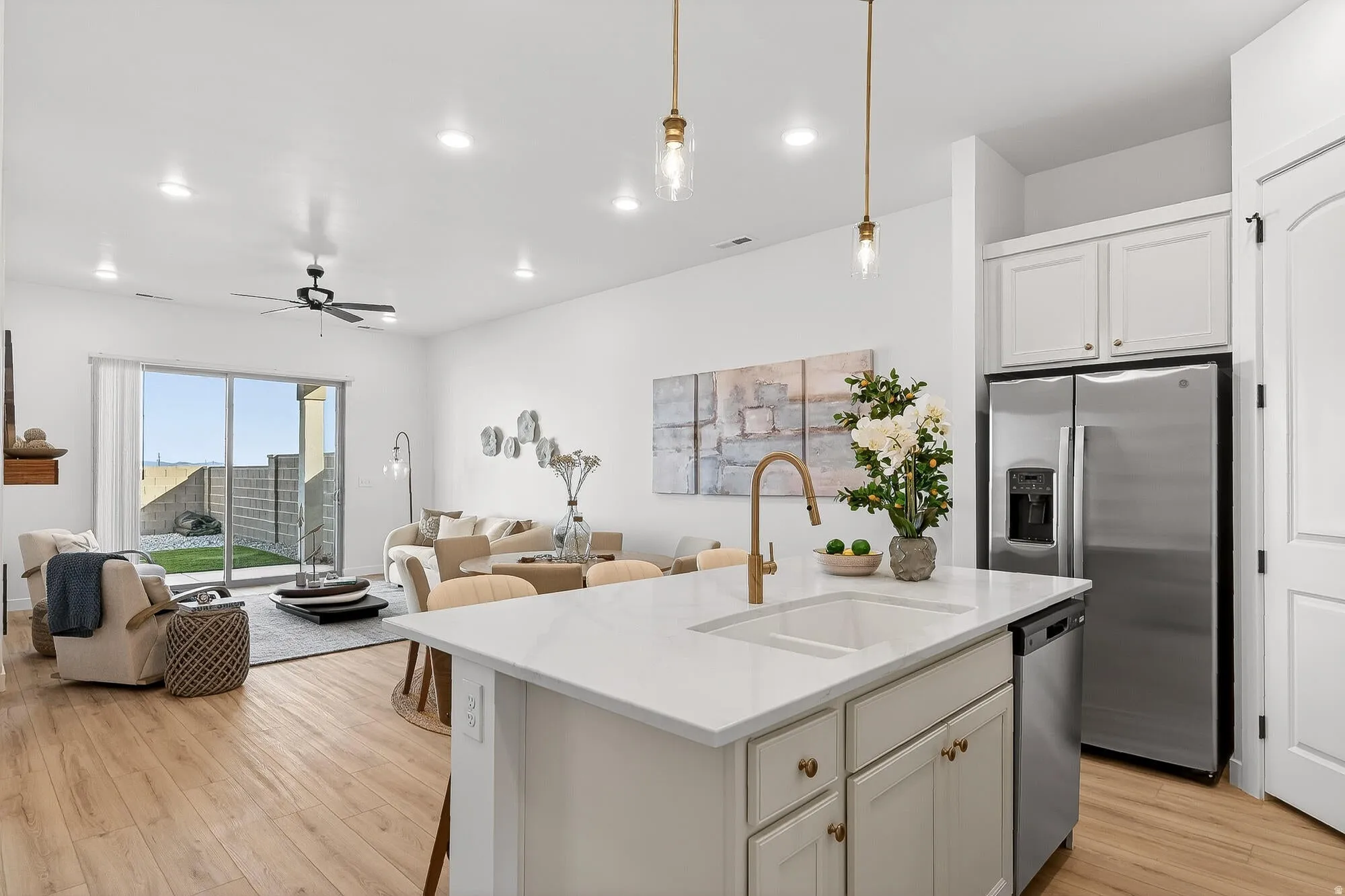 Kitchen featuring open floor plan, stainless steel appliances, an island with sink, white cabinetry, and a ceiling fan