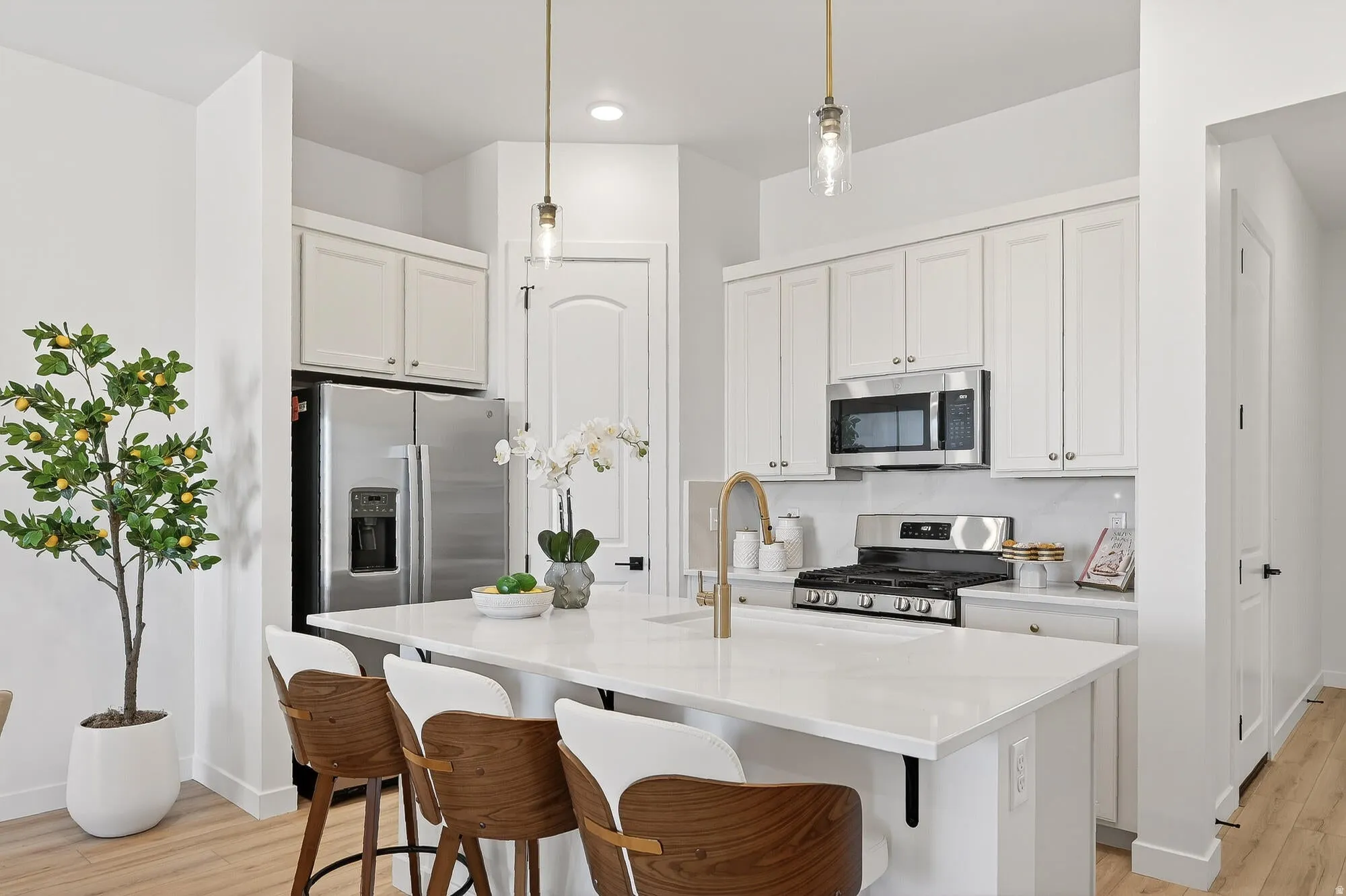 Kitchen with light wood finished floors, a kitchen bar, a center island with sink, and white cabinets