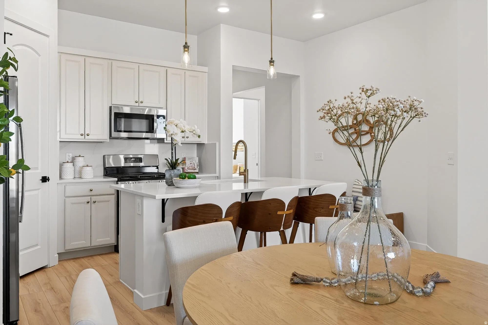 Kitchen featuring stainless steel appliances, light wood-type flooring, a kitchen breakfast bar, hanging light fixtures, and light stone counters