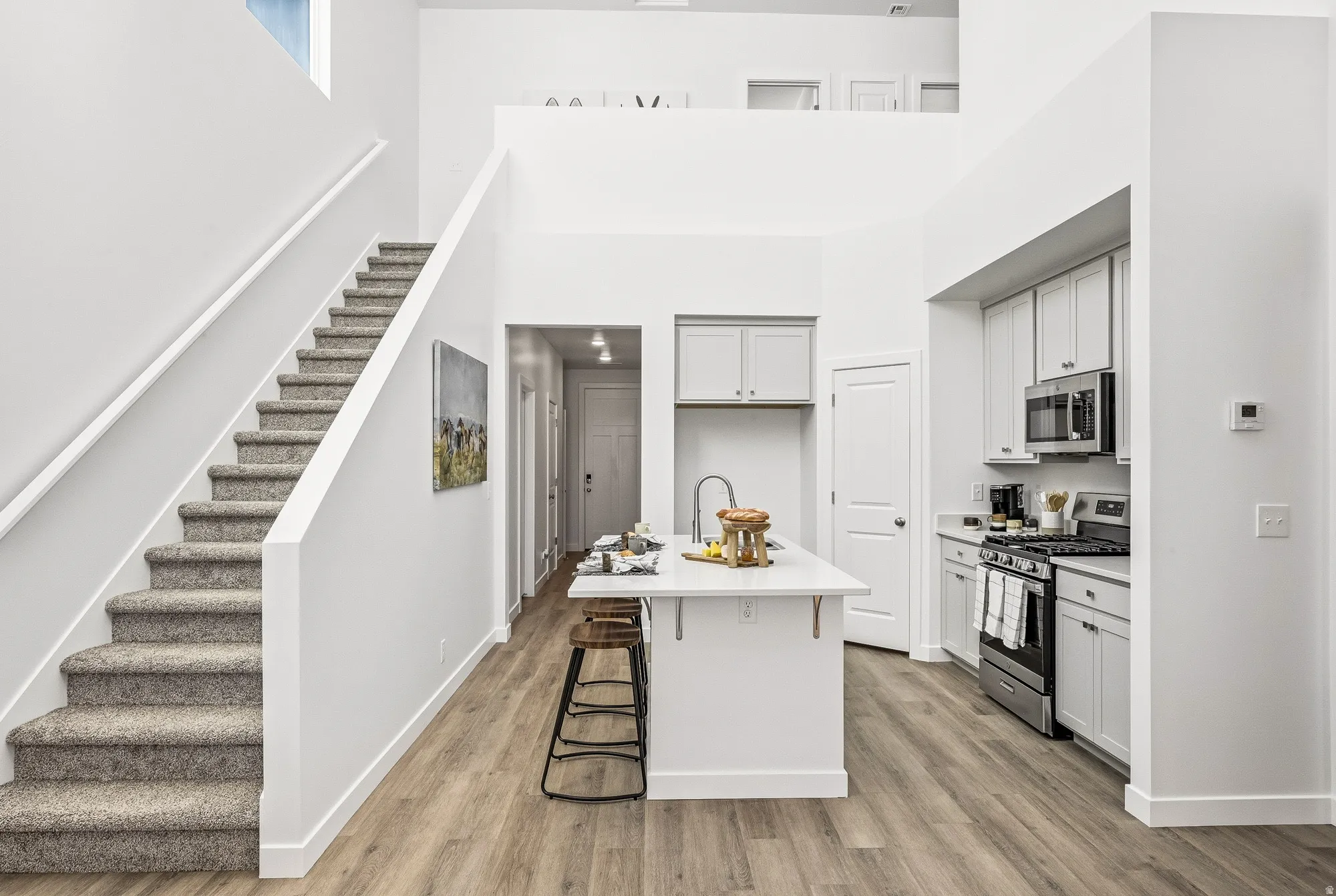 Kitchen featuring stainless steel appliances, a kitchen bar, a kitchen island with sink, light wood-type flooring, and light stone countertops