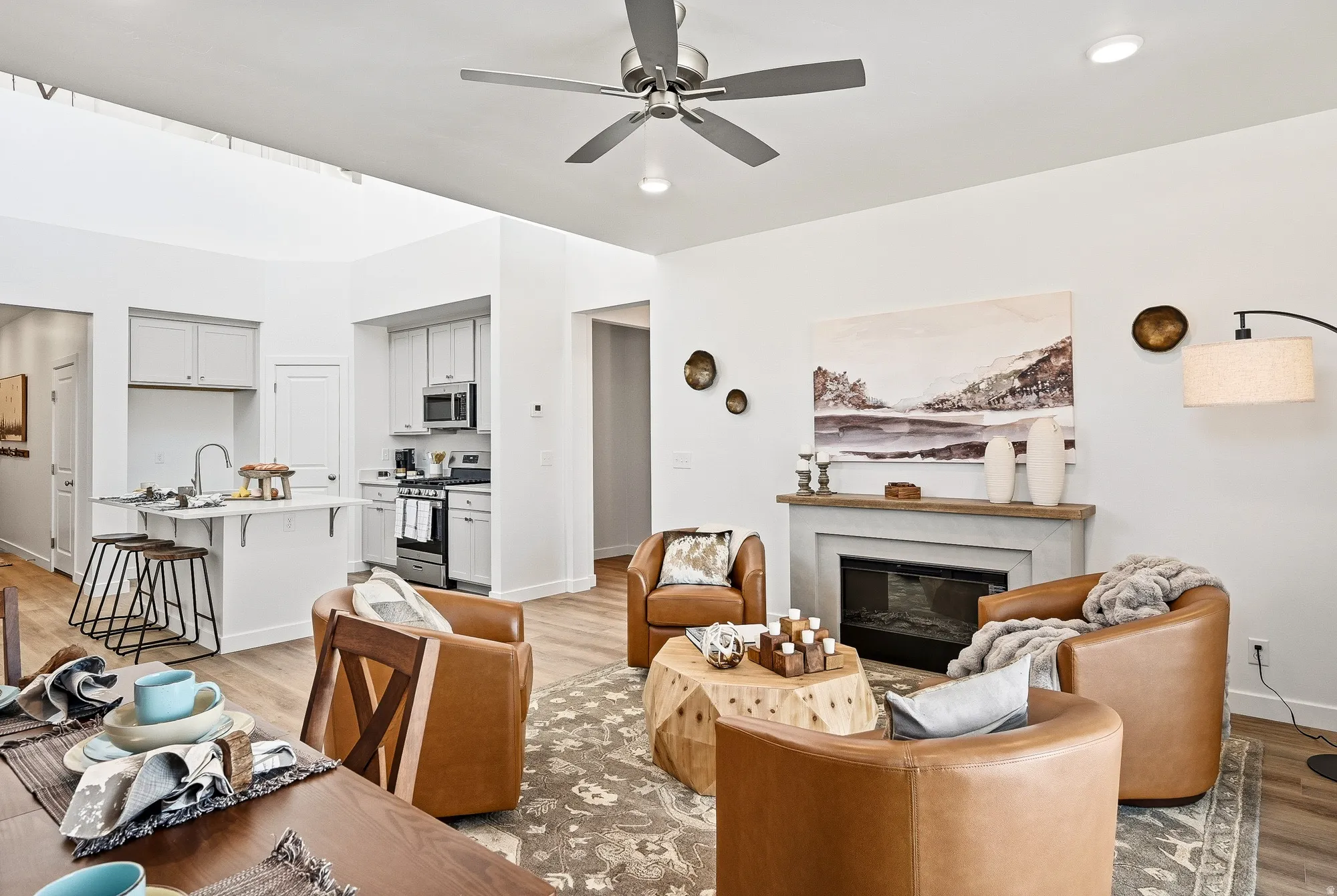 Living area featuring light wood-style floors, ceiling fan, and a glass covered fireplace