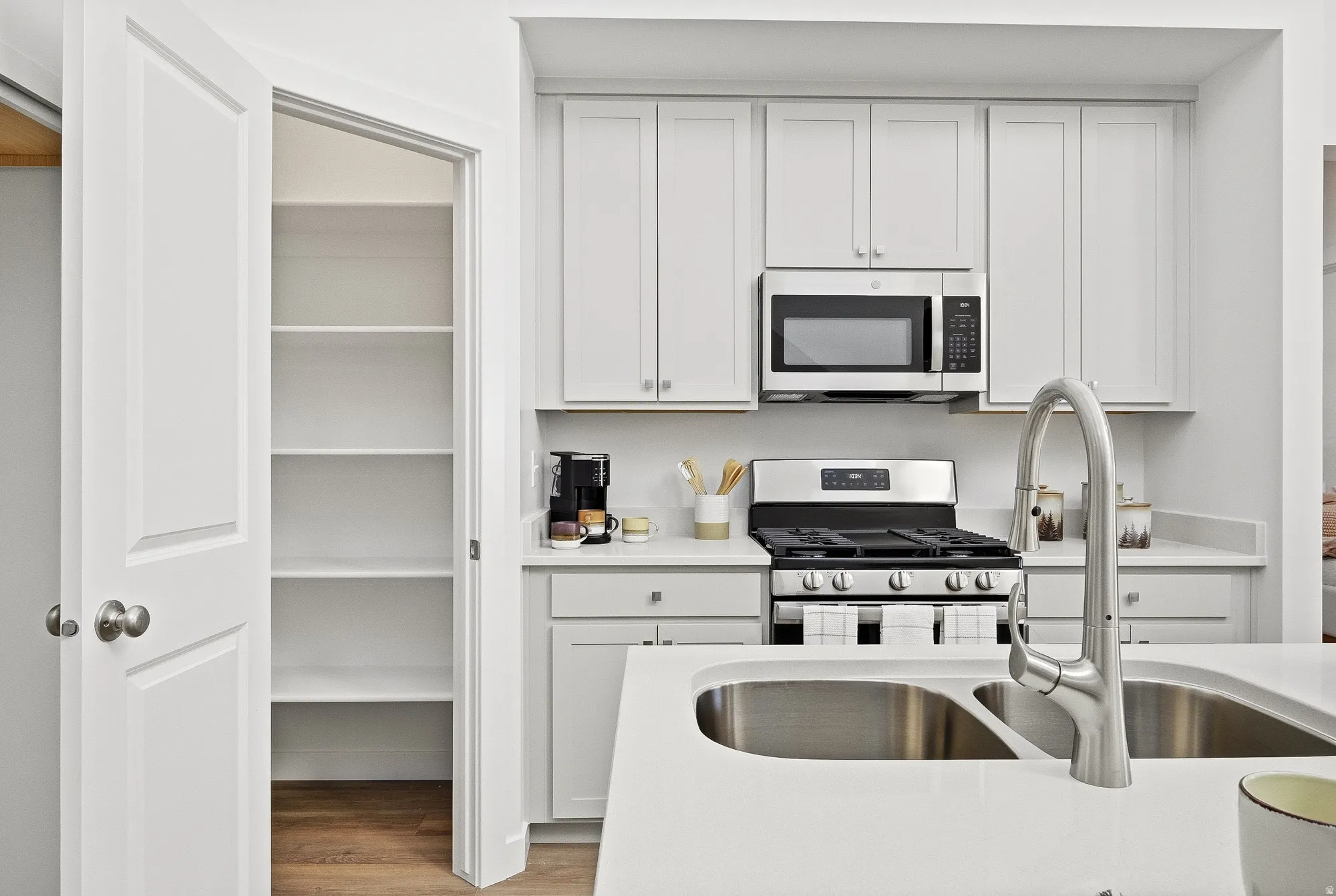 Kitchen with white cabinets, stainless steel appliances, light wood-style floors, and light stone counters