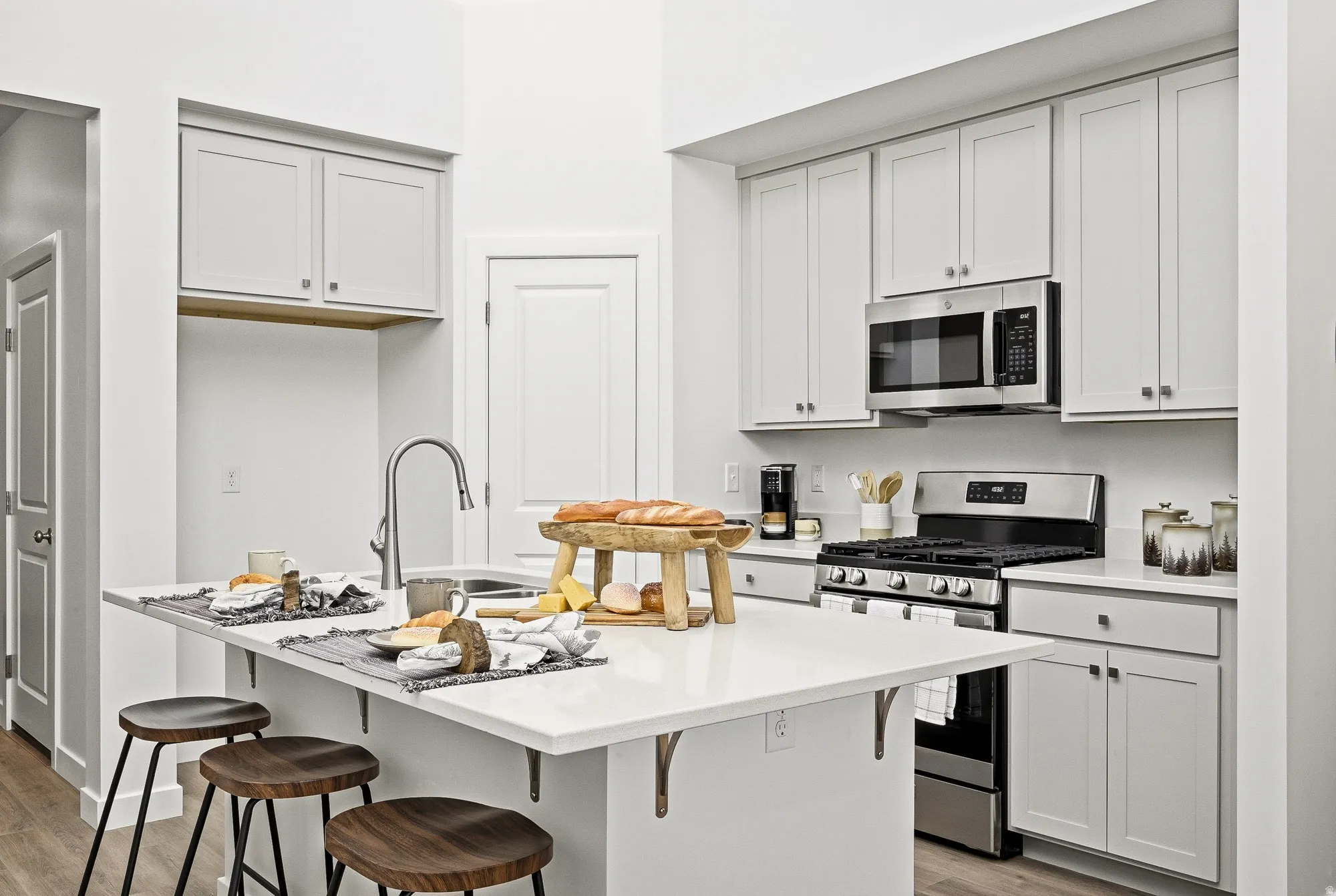 Kitchen with stainless steel appliances, a kitchen island with sink, white cabinetry, light wood-style flooring, and a breakfast bar area