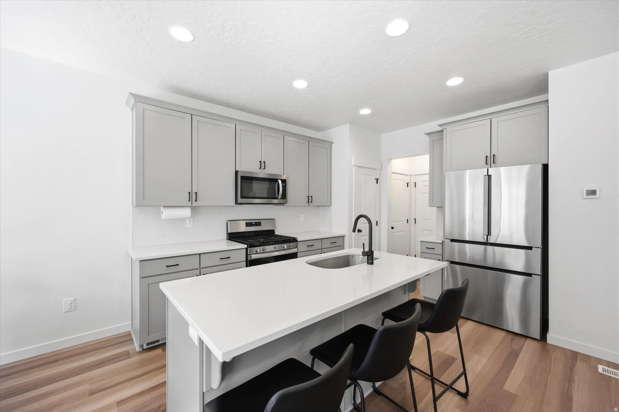 Kitchen featuring stainless steel appliances, gray cabinets, a breakfast bar, light wood finished floors, and recessed lighting