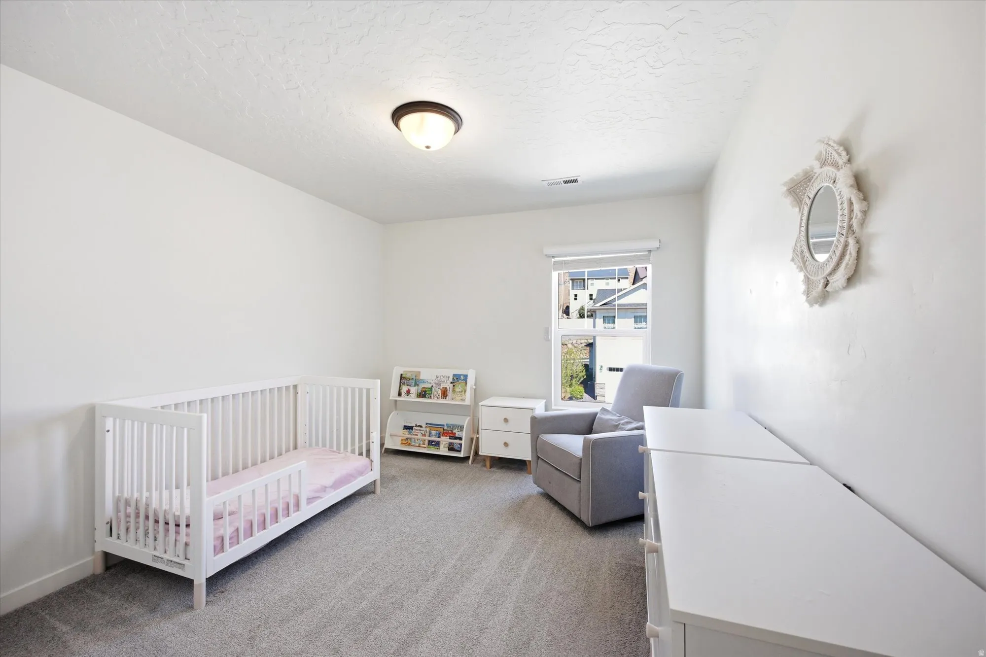 Bedroom with a crib, light carpet, and a textured ceiling