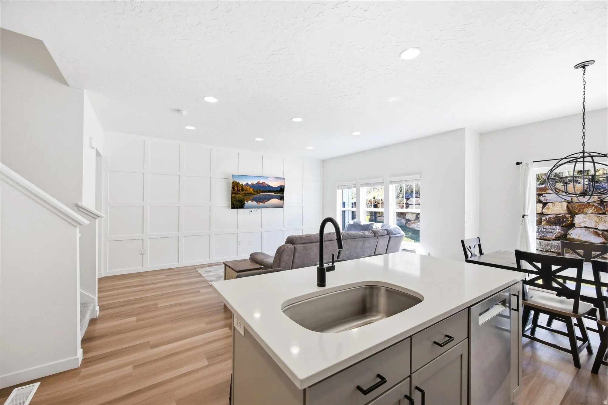 Kitchen featuring open floor plan, a center island with sink, light wood-style floors, light stone countertops, and hanging lights