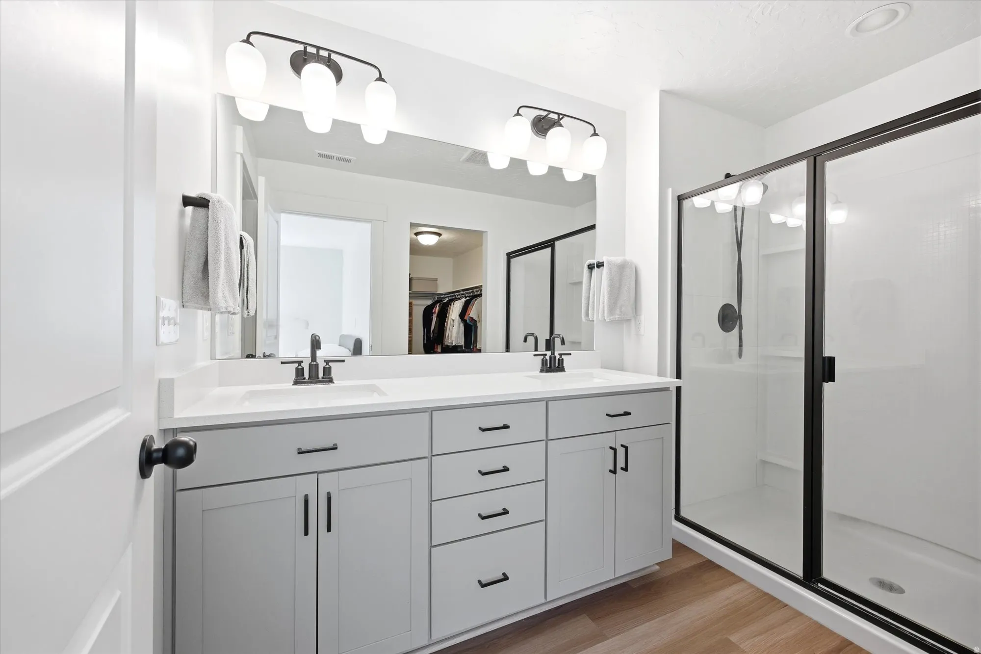 Full bathroom with double vanity, a stall shower, light wood-style floors, and a spacious closet