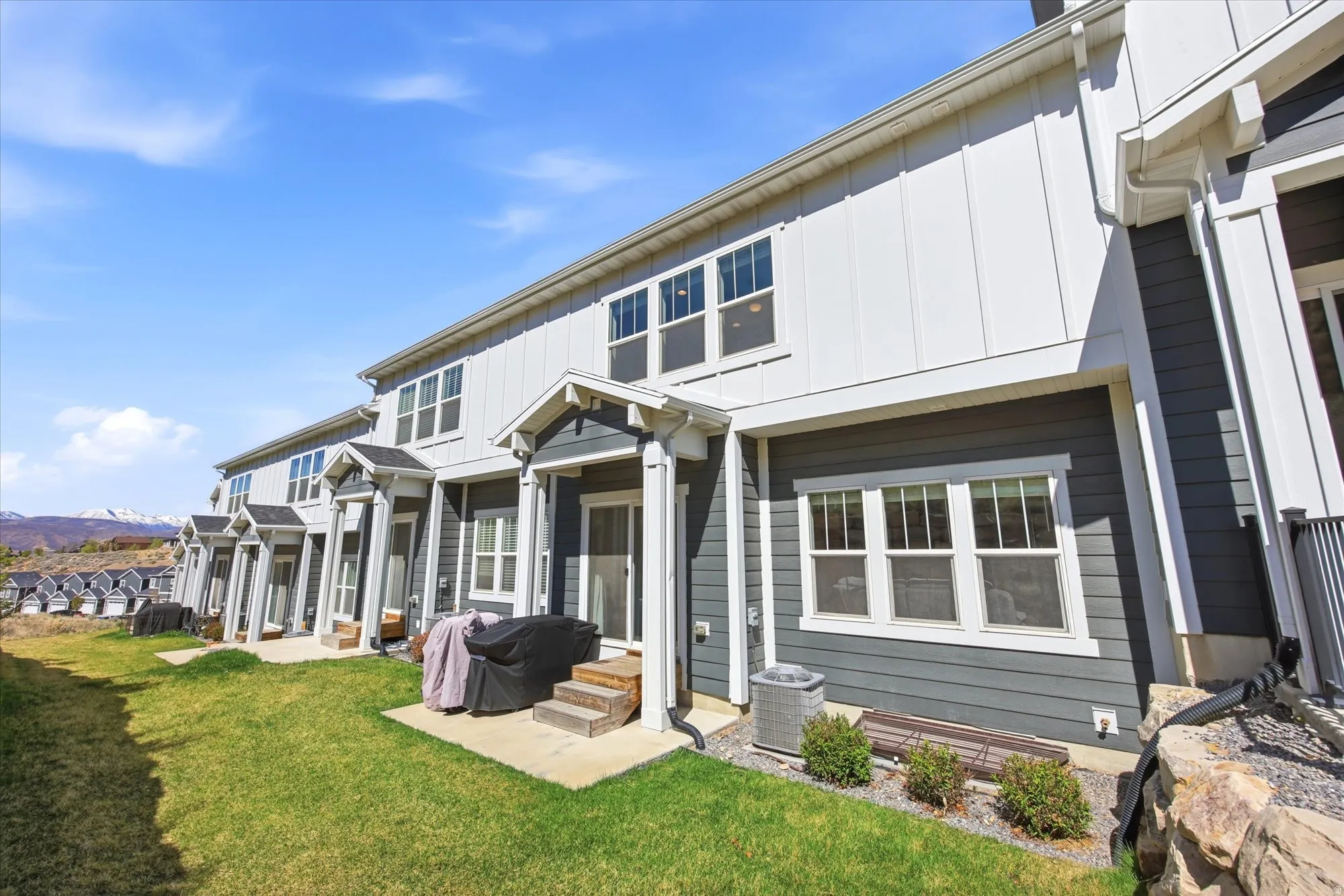 Back of property featuring board and batten siding, a patio area, a lawn, and a mountain view