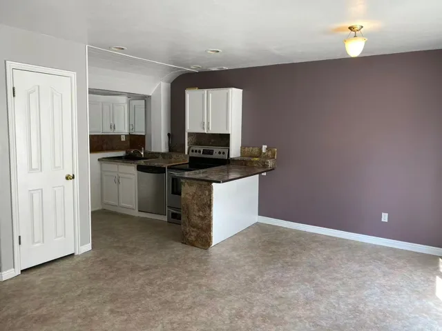 Kitchen with stainless steel appliances, a peninsula, a kitchen breakfast bar, white cabinets, and lofted ceiling