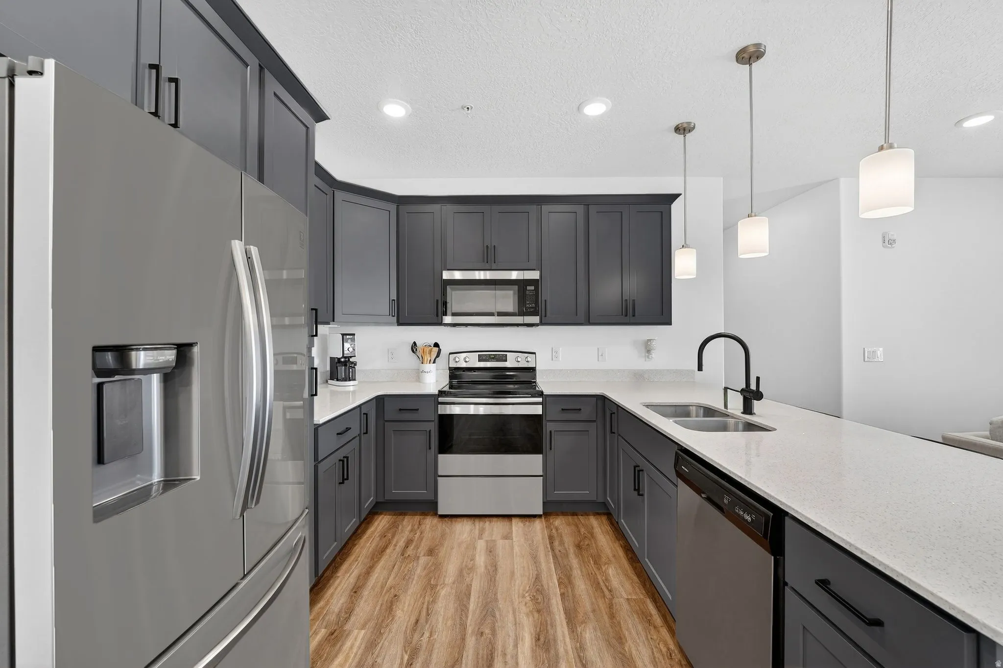 Kitchen with stainless steel appliances, light stone countertops, light wood-style flooring, gray cabinets, and hanging light fixtures