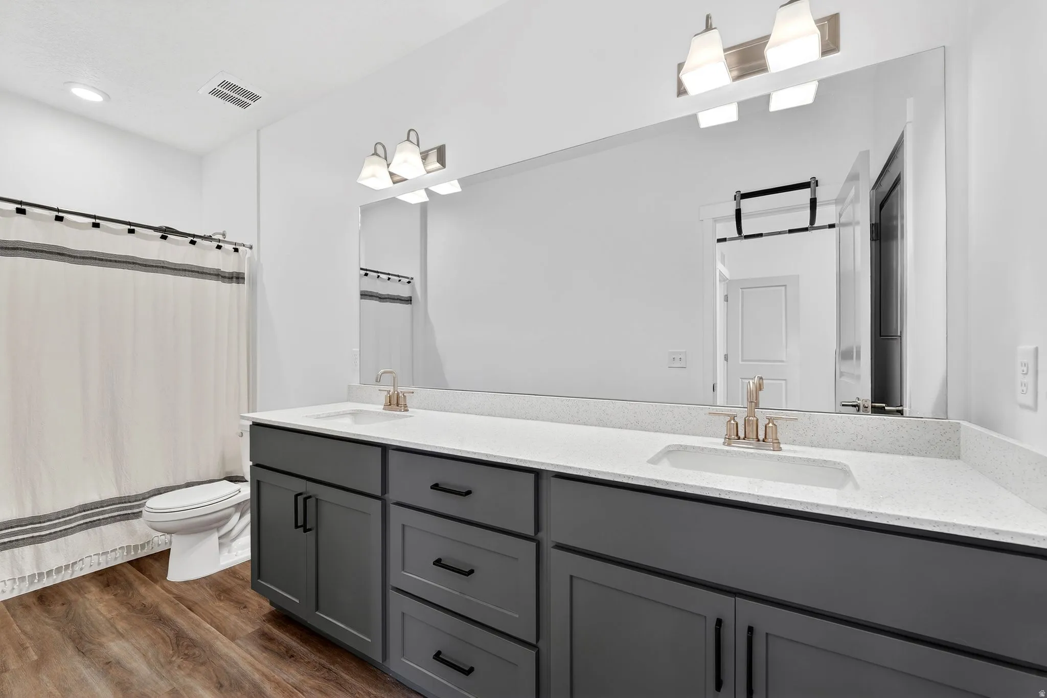 Full bath with double vanity, a shower with curtain, and dark wood-style flooring
