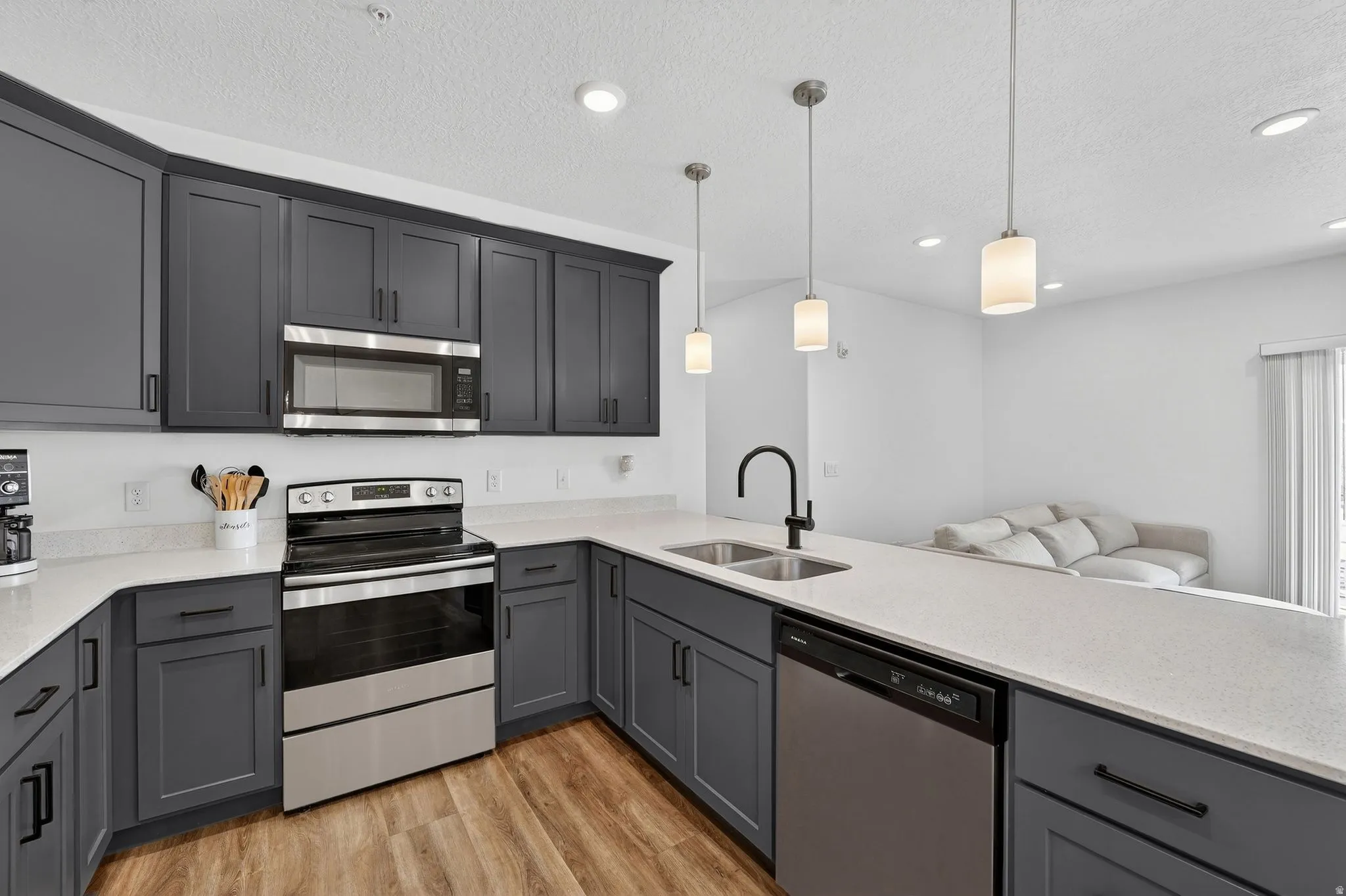 Kitchen featuring stainless steel appliances, light wood-style floors, gray cabinets, light stone counters, and a textured ceiling