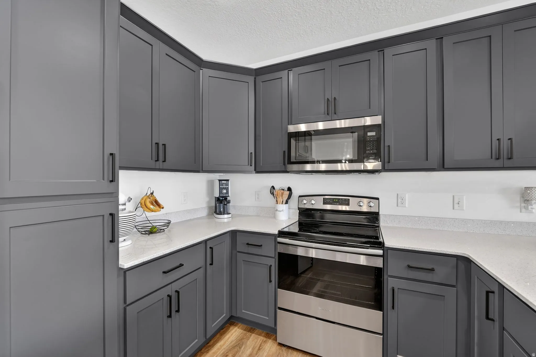 Kitchen with stainless steel appliances, gray cabinetry, light wood-style floors, a textured ceiling, and light stone countertops