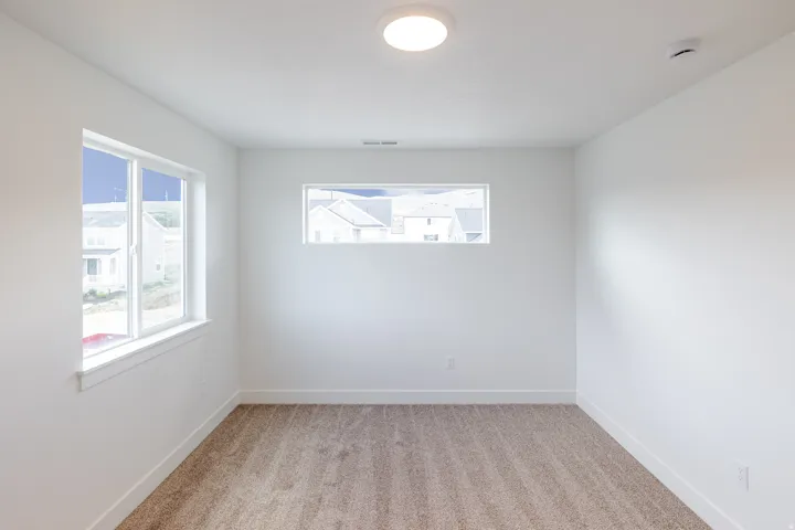 Bright room featuring white walls, a large window, a smaller horizontal window, and neutral-toned carpeting