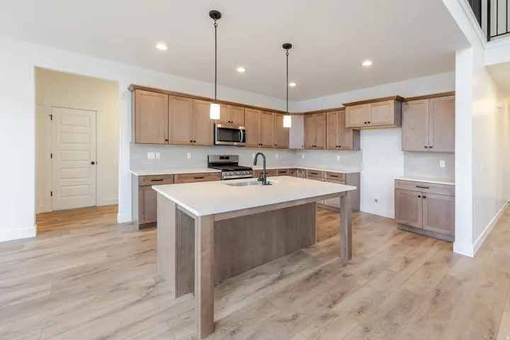 Kitchen featuring light wood-finish cabinetry, light countertops, stainless steel appliances, and a central island with a sink and pendant lighting