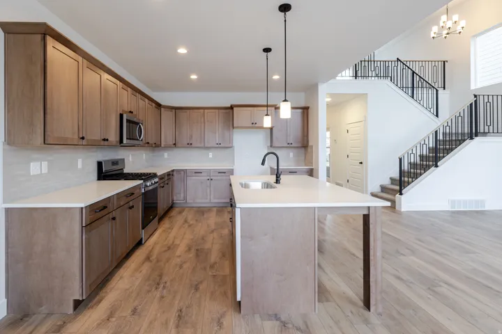 Open-concept kitchen featuring wood-finish flooring, light wood cabinetry with dark hardware, stainless steel appliances, and white countertops