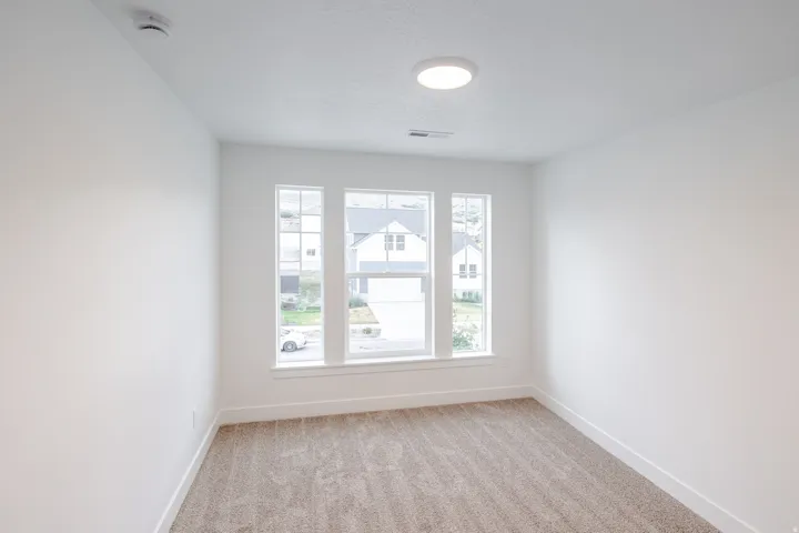 Bright interior room featuring a triple window, neutral carpet flooring, white walls, and a contemporary ceiling light fixture