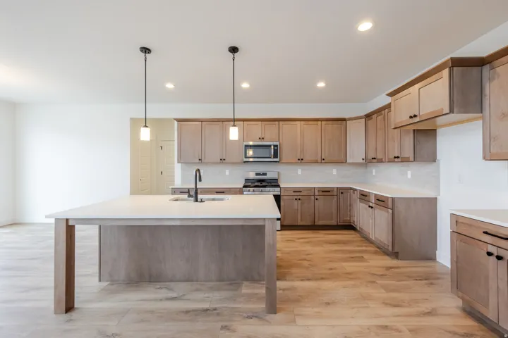 Kitchen featuring a central island with a sink and pendant lighting, wood-finish flooring, a full suite of stainless steel appliances, extensive cabinetry, and light-toned countertops