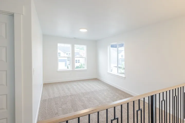 Carpeted loft space featuring multiple windows, recessed lighting, a paneled door, and a black metal and wood railing
