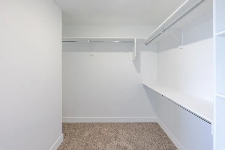 Spacious walk-in closet featuring white walls, white shelving, and metal hanging rods