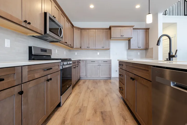 Modern kitchen featuring light wood-finish cabinetry, stainless steel appliances, light countertops, a tile backsplash, and wood-finish flooring