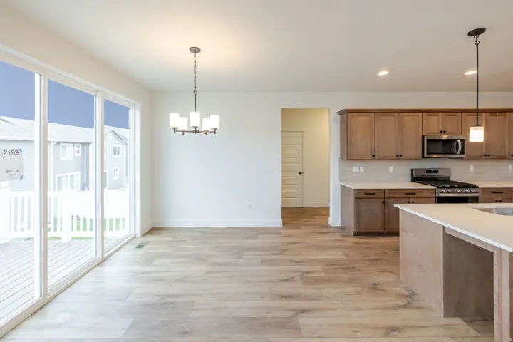 Spacious open-concept living area featuring wood-finish flooring, a contemporary chandelier, and expansive sliding glass doors
