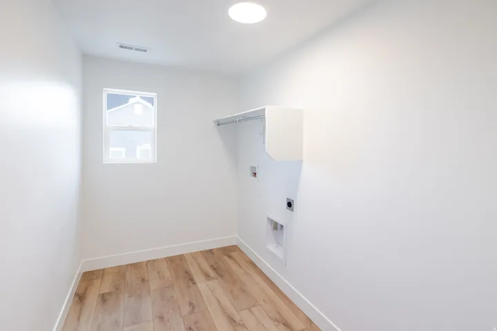 Dedicated utility space featuring wood-finish flooring, a single window, white walls, built-in shelving, and appliance hookups