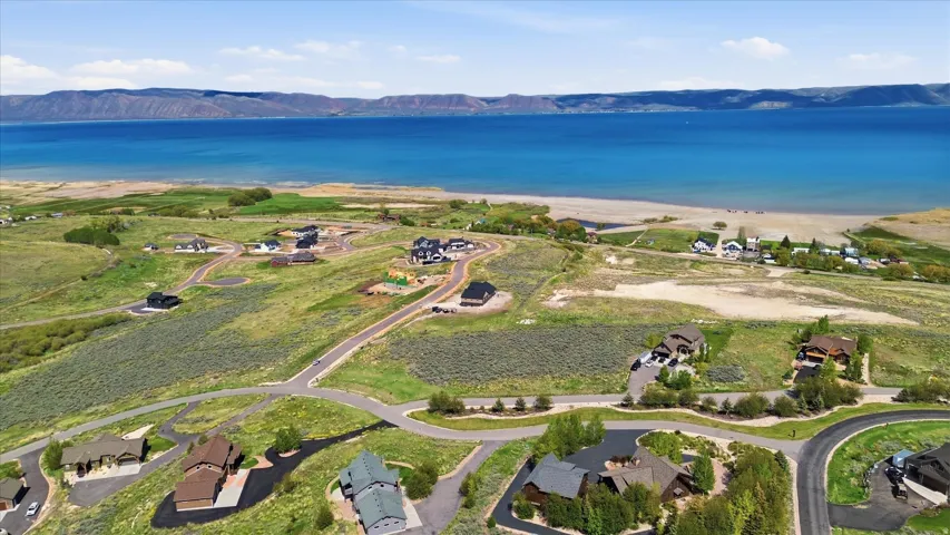 Aerial perspective showcasing numerous residential properties situated on a gently sloping landscape, with a large body of water and distant mountains forming a scenic backdrop