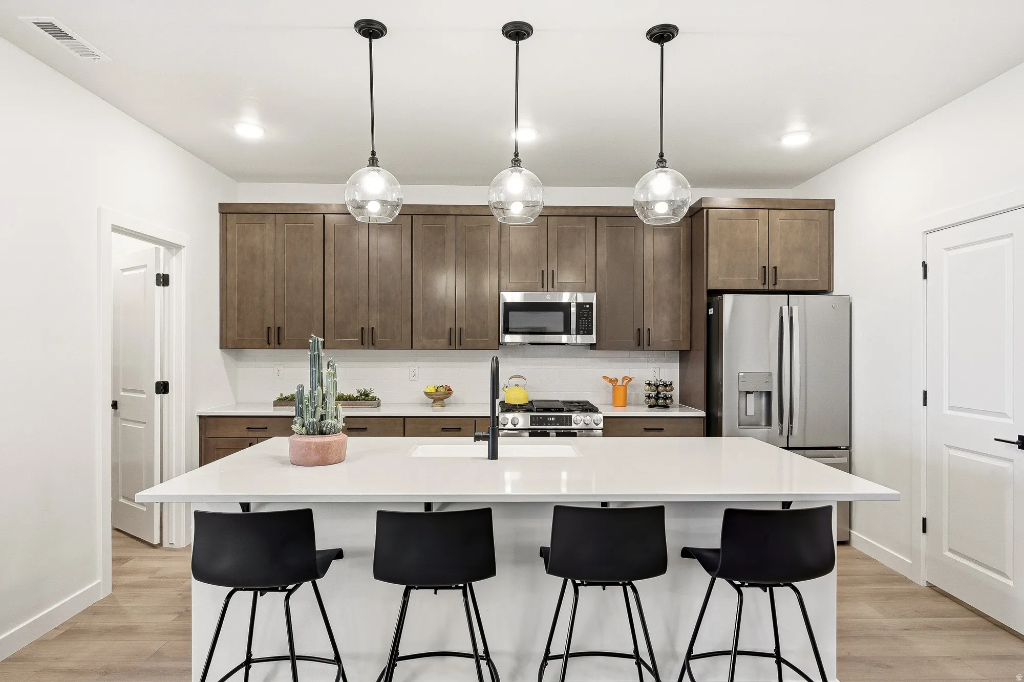 Kitchen with dark wood finish cabinets, a kitchen island with sink, decorative light fixtures, and stainless steel appliances