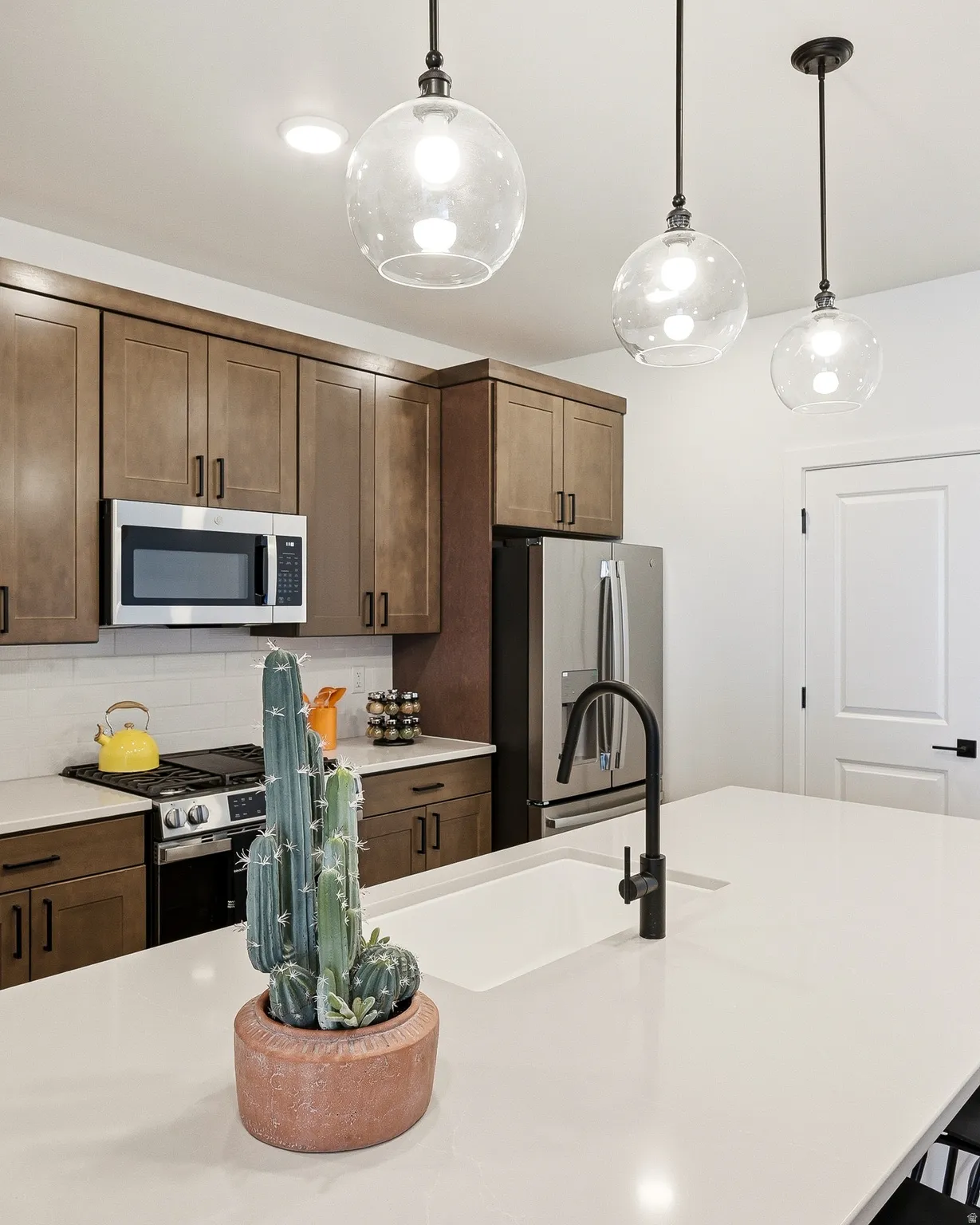 Kitchen featuring stainless steel appliances, backsplash, decorative light fixtures, light stone countertops, and dark wood finish cabinets