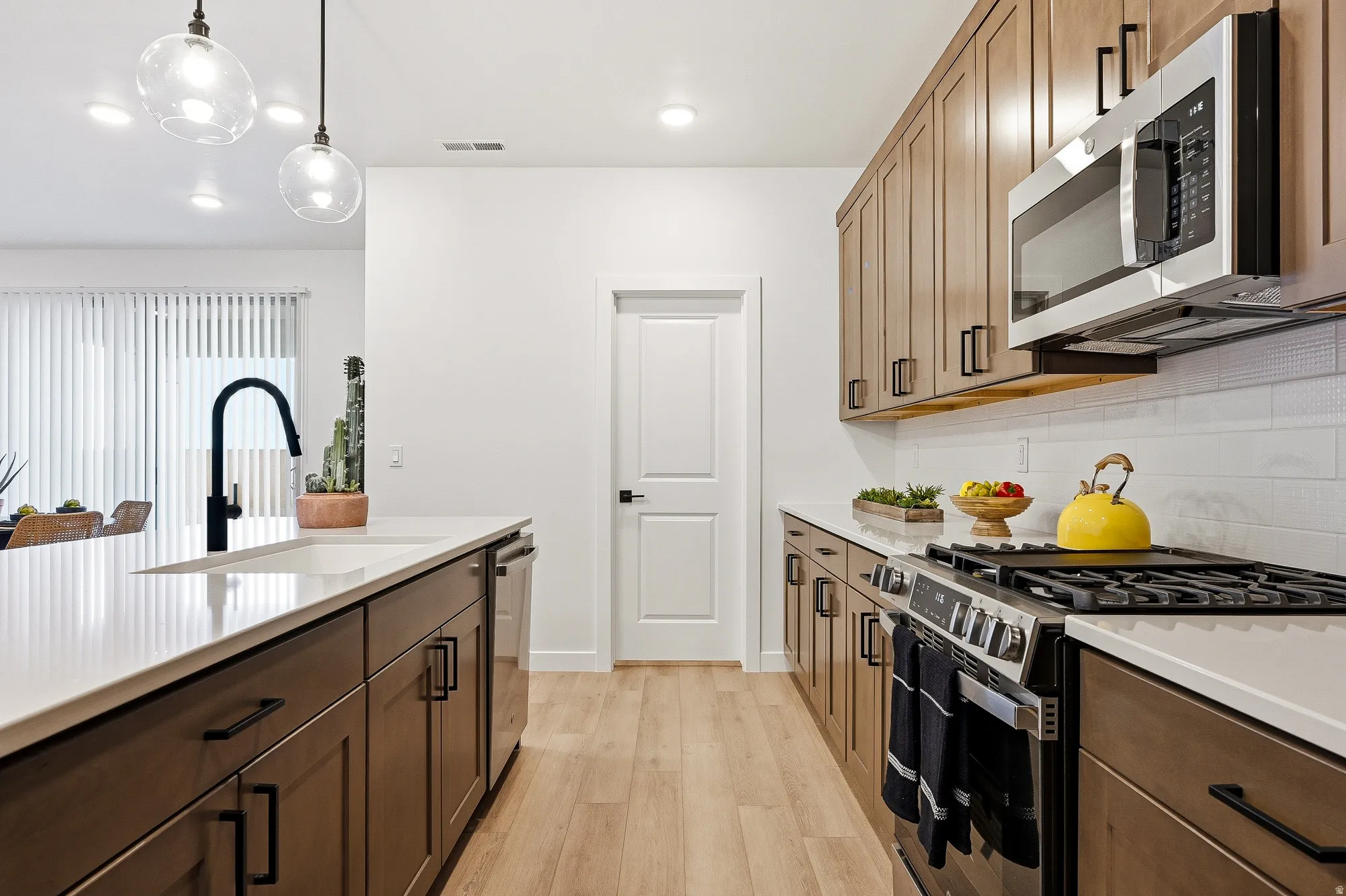 Kitchen with stainless steel appliances, light wood-style floors, light stone countertops, hanging light fixtures, and decorative backsplash