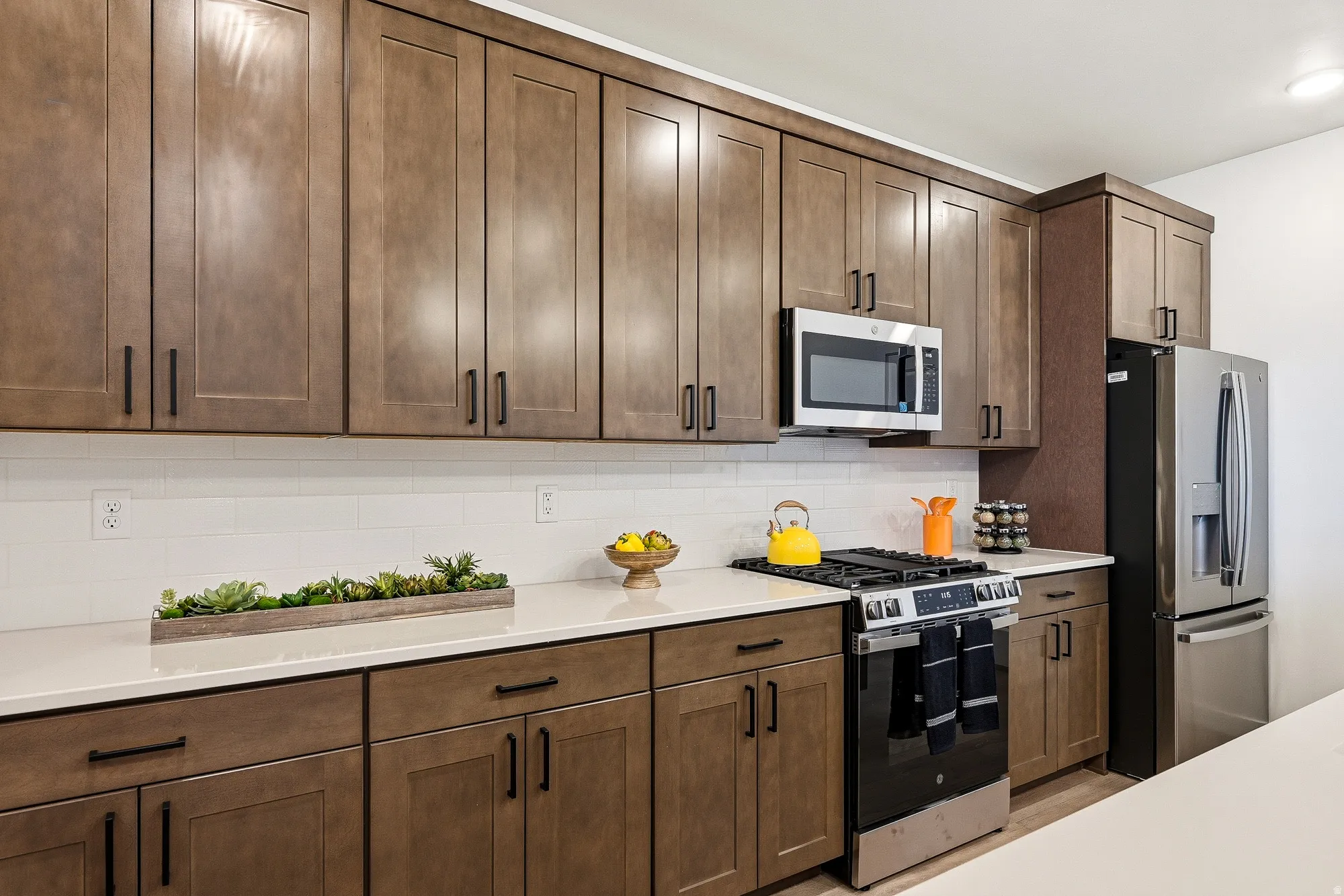 Kitchen featuring stainless steel appliances, tasteful backsplash, light stone countertops, and dark wood finish cabinets