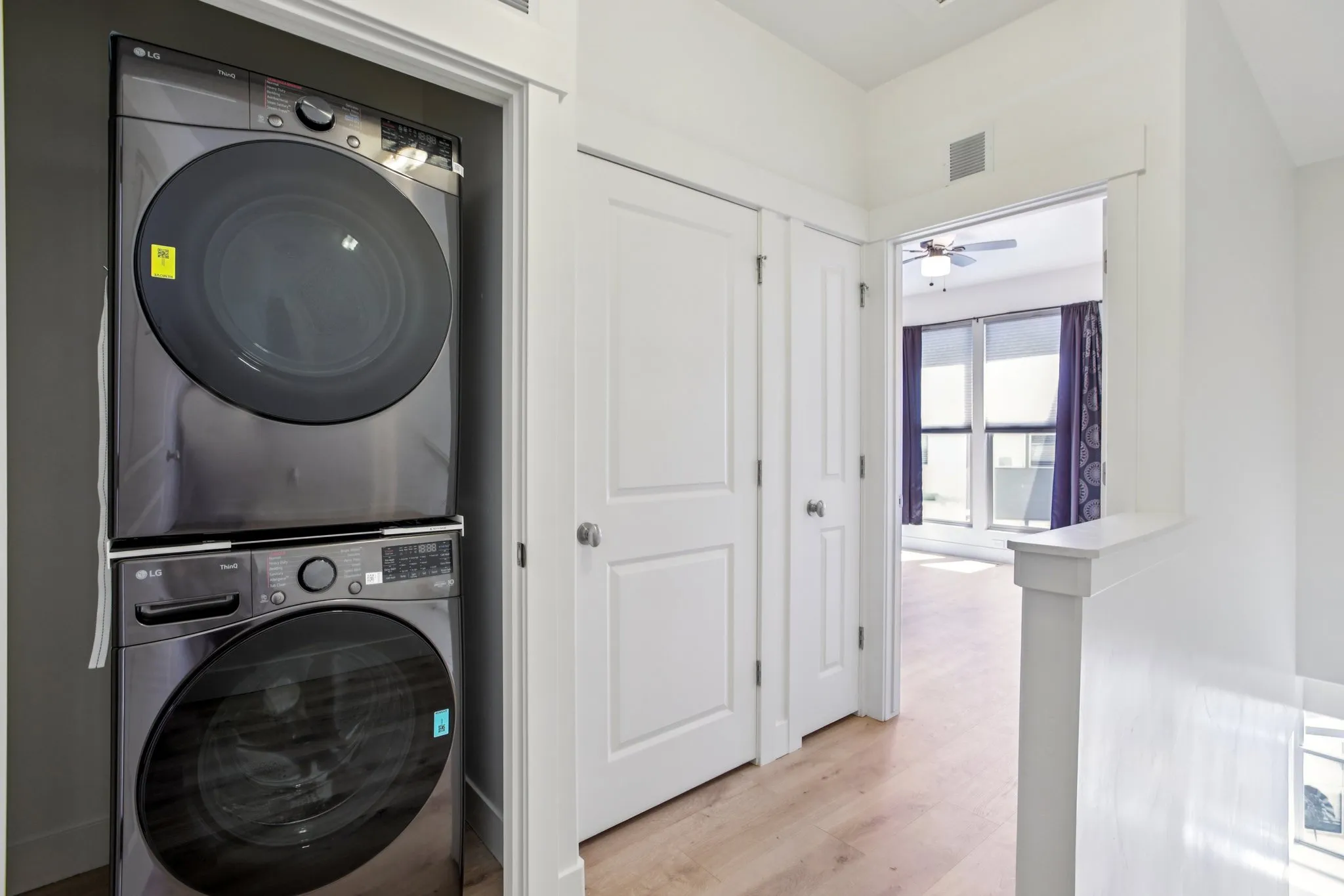 Laundry area with stacked washing machine and dryer, light wood-style floors, and ceiling fan