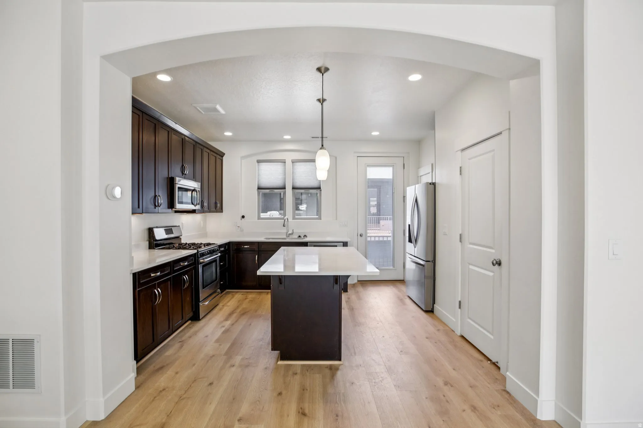 Kitchen featuring dark wood finish cabinets, stainless steel appliances, light wood-style floors, a center island, and arched walkways