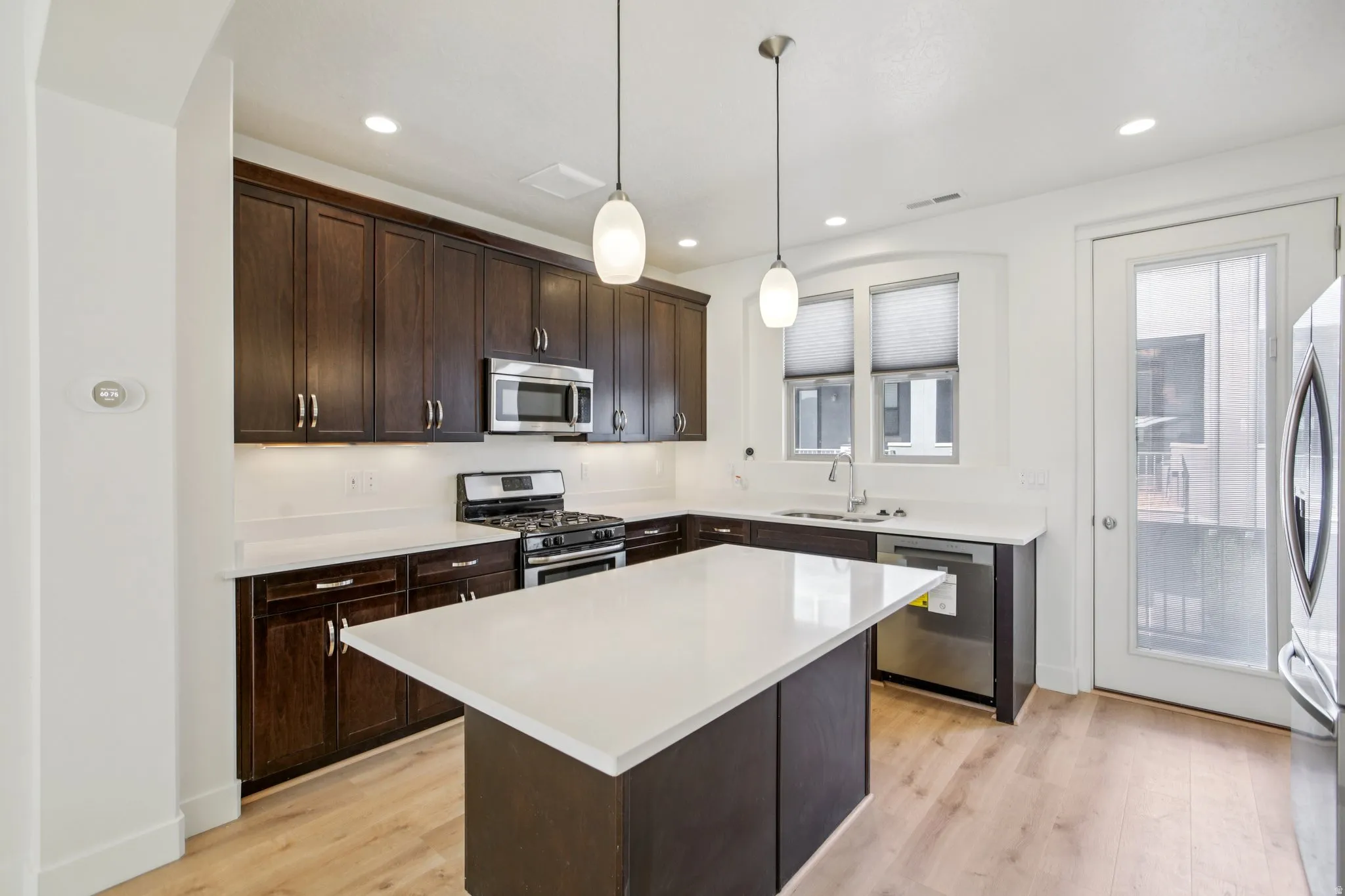 Kitchen with dark wood finish cabinetry, stainless steel appliances, a center island, decorative light fixtures, and light wood-type flooring