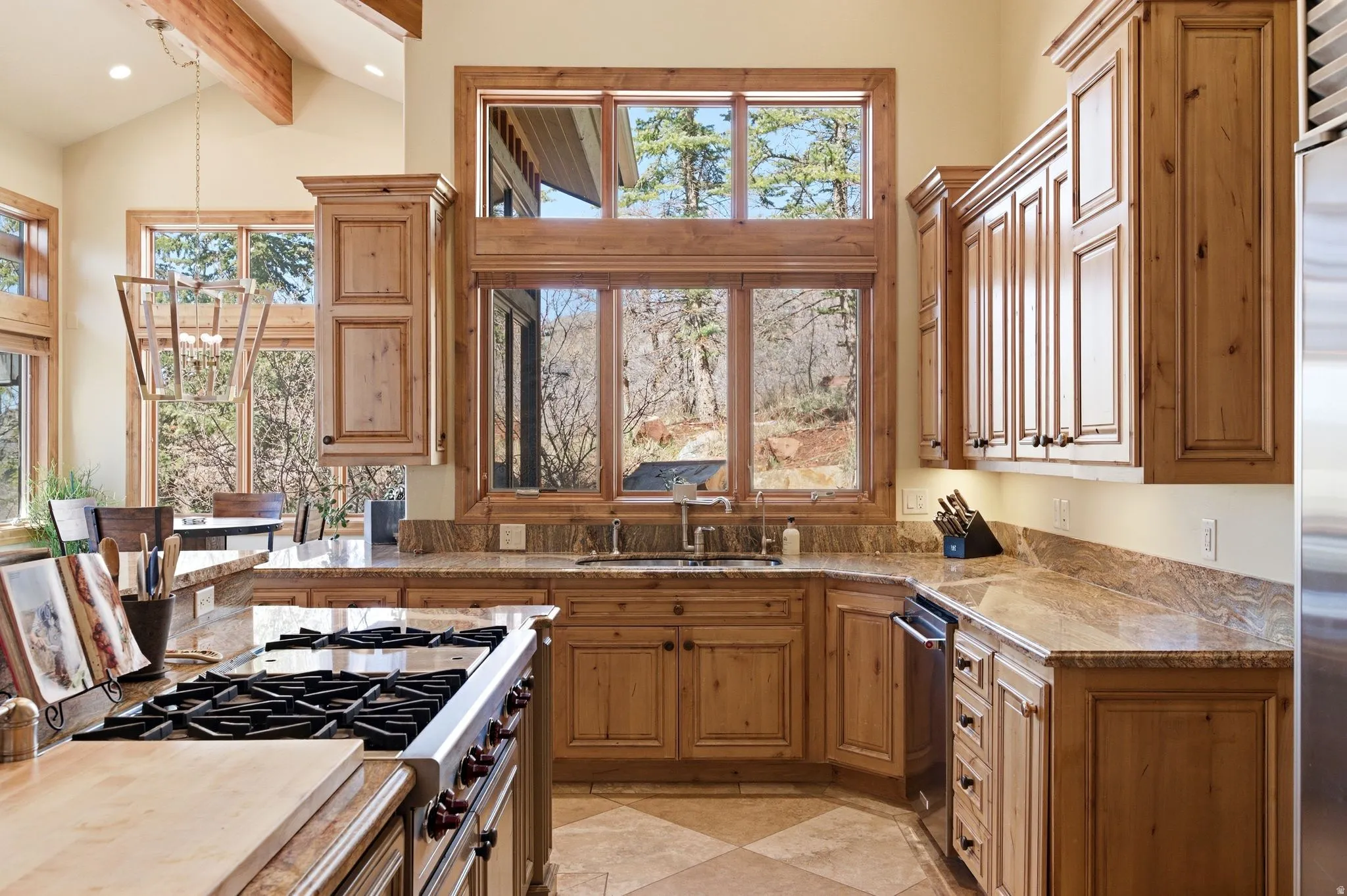 Kitchen featuring wood finish cabinets, stainless steel appliances, suspended lighting, lofted ceiling, and light stone countertops