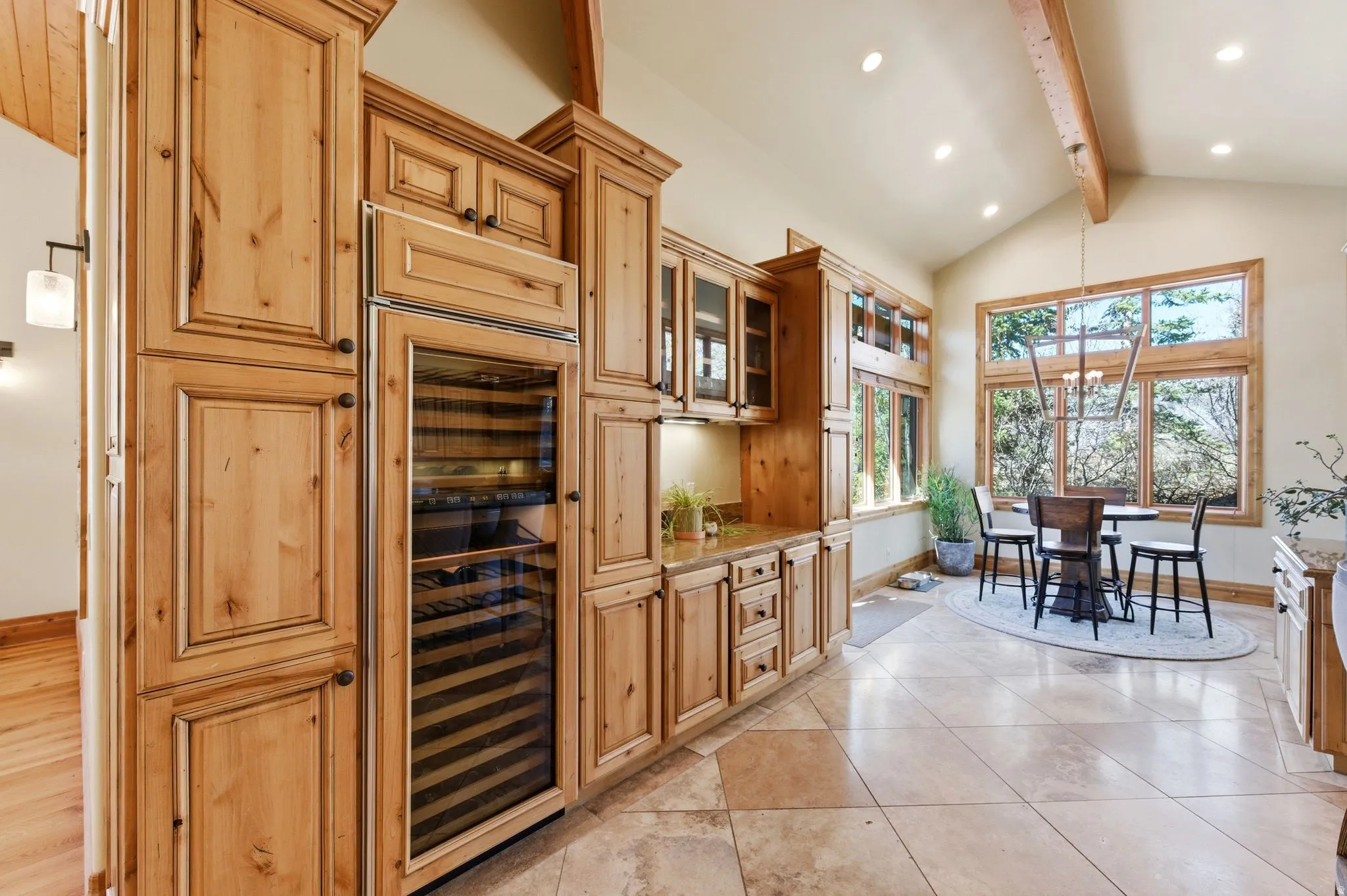 Kitchen with beverage cooler, glass fronted cabinets, vaulted ceiling, light stone counters, and a chandelier
