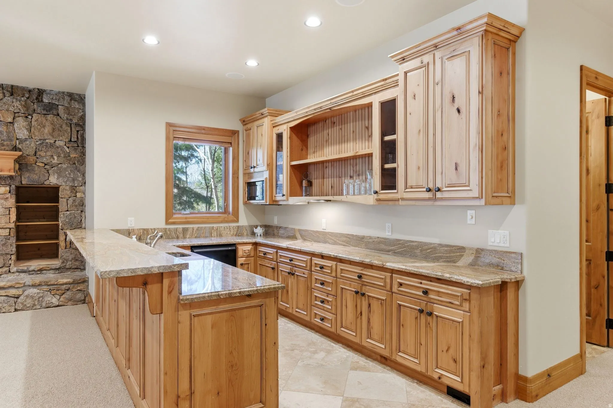 Kitchen with glass insert cabinets, open shelves, a kitchen bar, a peninsula, and light stone counters