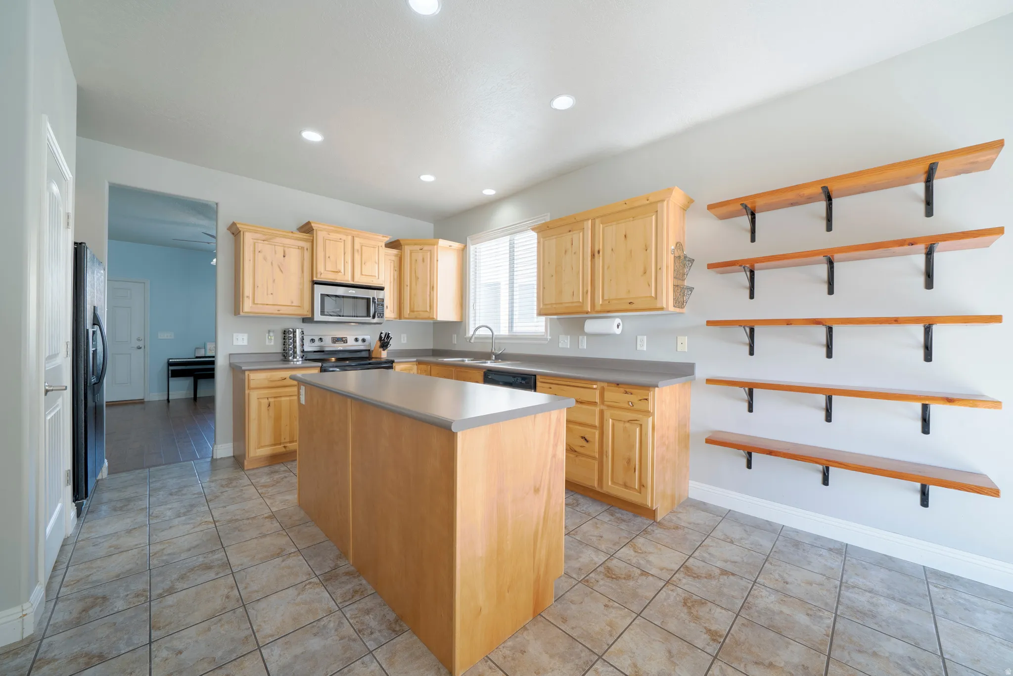 Kitchen with light wood finish cabinetry, open shelves, a center island, stainless steel appliances, and light tile patterned flooring