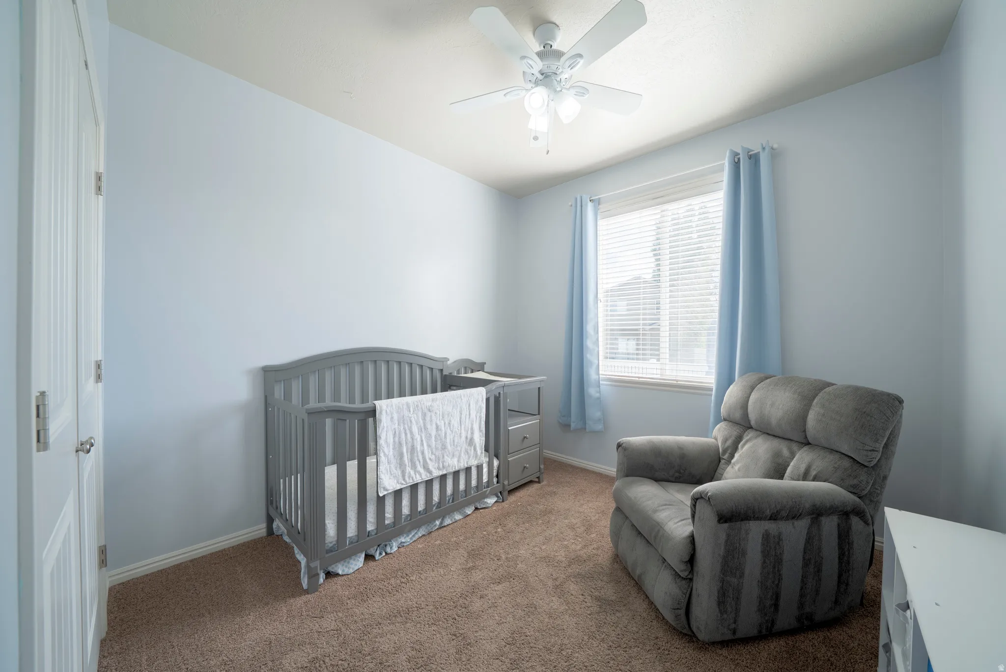 Carpeted bedroom featuring a crib and a ceiling fan