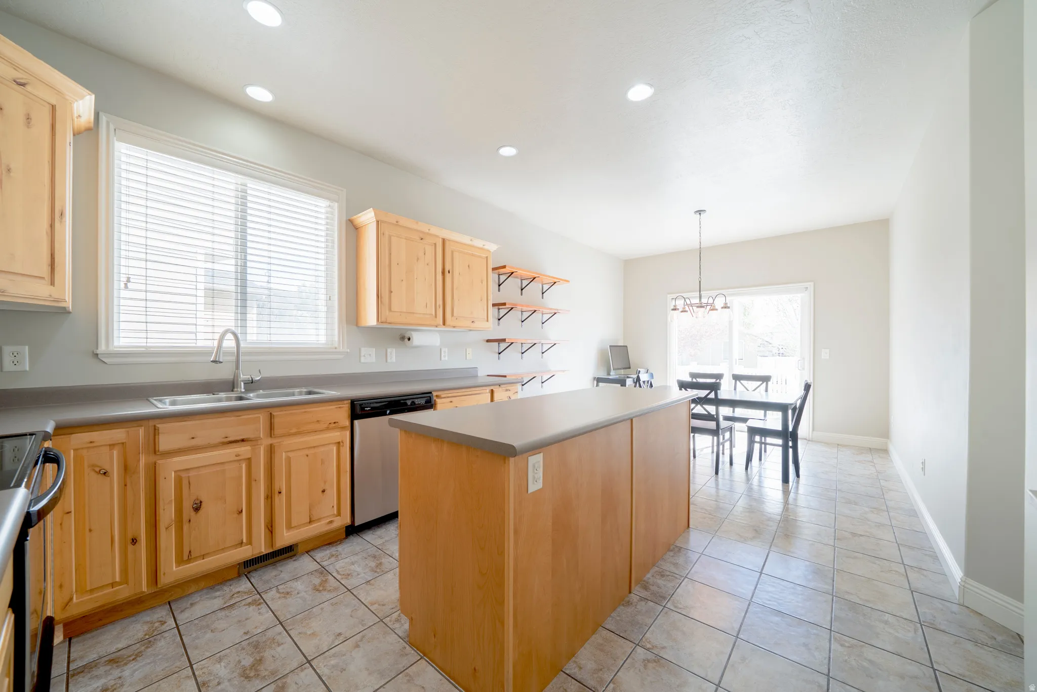 Kitchen featuring light wood finish cabinets, a kitchen island, light tile patterned flooring, and stainless steel appliances