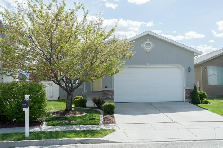 View of front of home featuring an attached garage, stone siding, driveway, and stucco siding