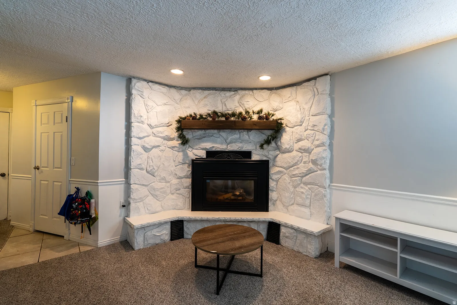 Living area with a stone fireplace, a textured ceiling, light colored carpet, and recessed lighting