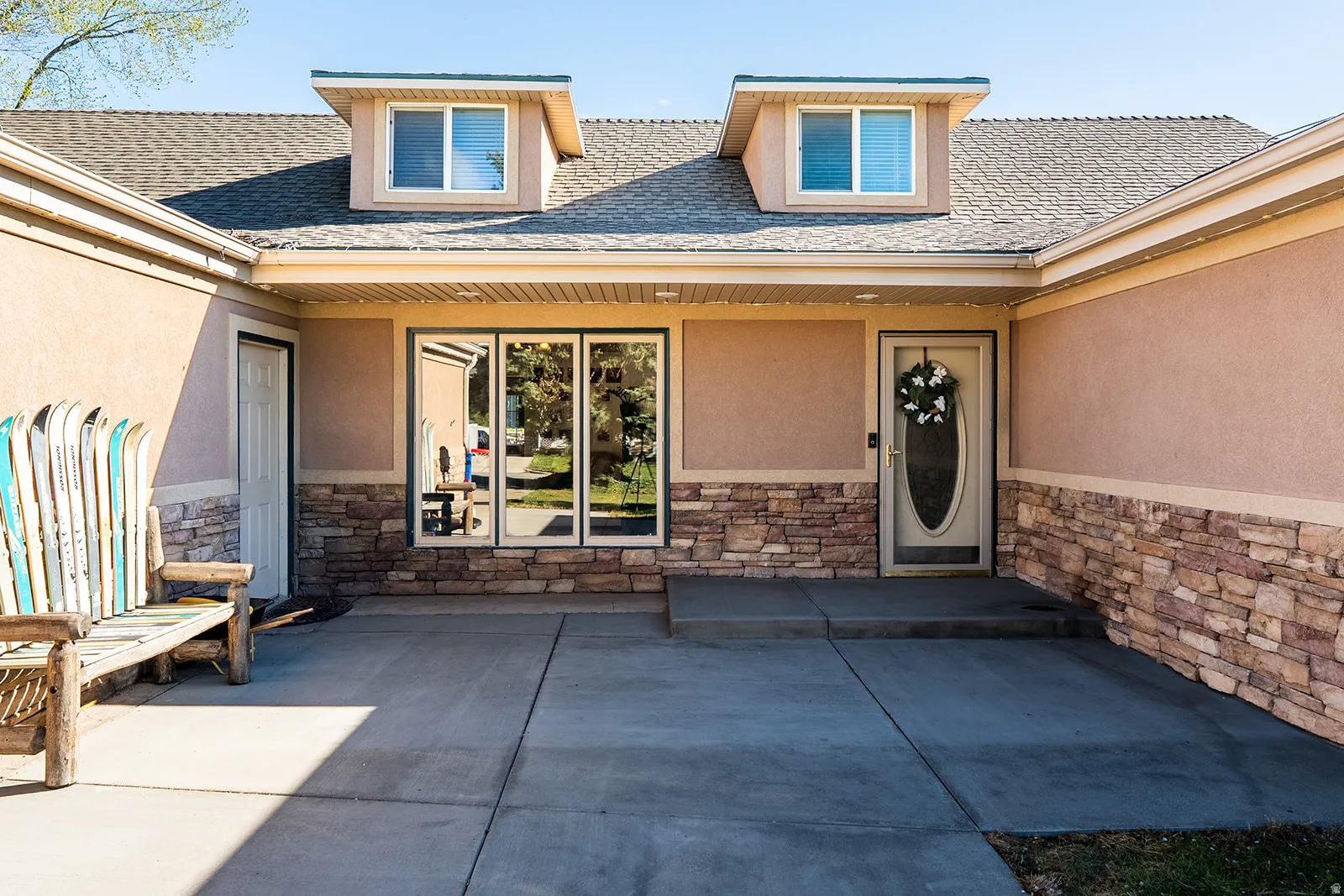Property entrance with stone siding, stucco siding, a shingled roof, and covered porch