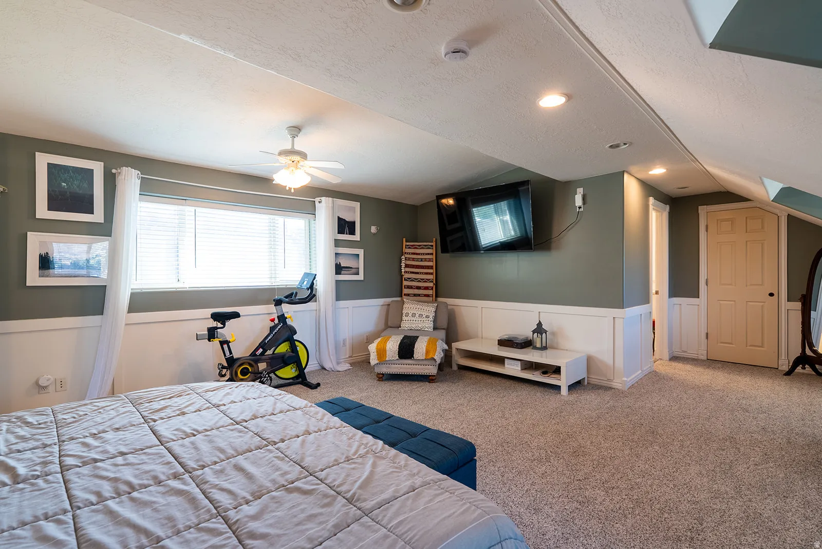 Carpeted bedroom with a wainscoted wall, ceiling fan, and a decorative wall